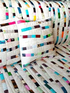 two pillows are sitting on top of a quilted bed spread with multicolored squares