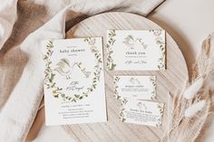 three wedding stationery items on a wooden plate with white linen and greenery around them