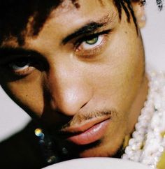 a close up of a man with green eyes and pearls around his neck holding a plate