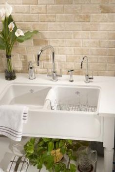 a white sink sitting under a window next to a vase filled with flowers and greenery