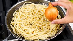 a person is holding an onion over some noodles in a pan on the stove top