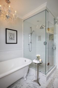 a white bath tub sitting under a chandelier next to a walk in shower