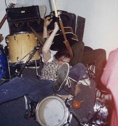 a man laying on the floor with his head in an open drum kit and other musical instruments behind him