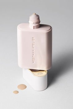 an empty pink bottle sitting on top of a white table next to two round dots