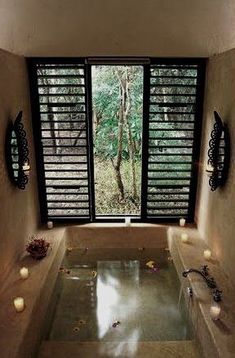 an indoor jacuzzi tub with candles on the side and windows in the back