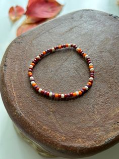 a beaded bracelet sitting on top of a piece of wood next to autumn leaves