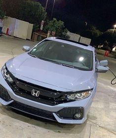 a blue honda civic is parked in a parking lot at night with people looking on