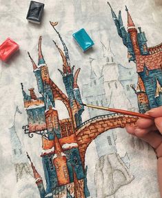 someone is painting a castle on a piece of fabric with some paint and pencils