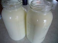 two jars filled with liquid sitting on top of a counter next to a bottle of milk