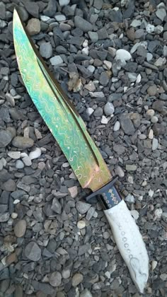 a knife laying on the ground with rocks and gravel in the backgroung