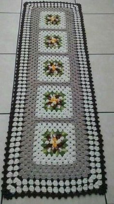 a crocheted table runner on the floor with flowers and leaves in it,