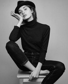 a woman sitting on top of a wooden table wearing black clothes and a fedora