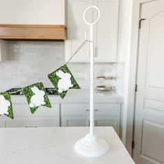 a white kitchen with green and white decorations on the counter top, hanging from a wire