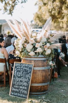 a wooden barrel filled with flowers sitting on top of a grass covered field next to a sign