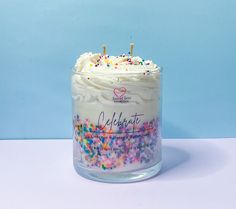 a cake in a glass jar with sprinkles on the top and candles sticking out of it