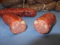 three sausages on a blue table next to some potatoes and other food items in the background