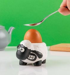 a hand is holding a spoon over an egg shaped like a sheep