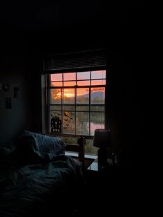 a bedroom with a window that has the sun going down in the sky over mountains