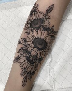 a sunflower tattoo on the arm with leaves and petals in it's center