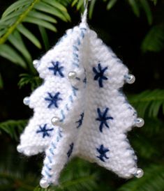 a crocheted christmas tree ornament hanging from a pine tree branch with blue and white snowflakes on it