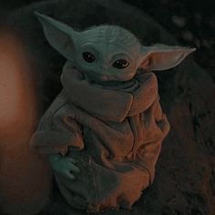 a baby yoda doll sitting on top of a rock next to a lit candle