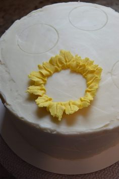 a white cake with yellow icing and a flower decoration on the top, sitting on a table