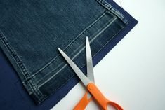 a pair of scissors sitting on top of a piece of fabric next to a pair of jeans