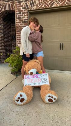 two girls standing next to a large teddy bear with a sign that says i almost love you