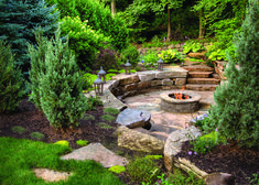 an outdoor fire pit surrounded by trees and rocks in the middle of a garden area