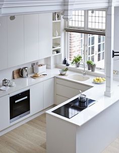 a kitchen with white cabinets and an island in front of a window that has potted plants on it