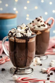 two hot chocolate drinks with marshmallows and candy canes on the side