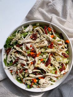 a white bowl filled with chicken salad on top of a gray cloth next to a spoon