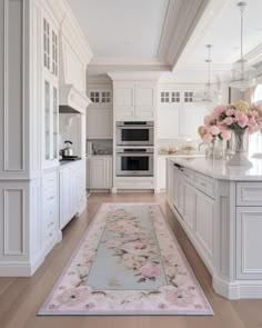 a large kitchen with white cabinets and pink flowers on the rug in front of the stove