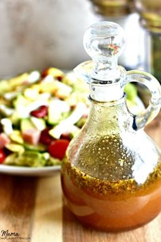 a glass bottle filled with dressing next to a plate of salad on a wooden table