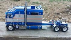 a blue and silver toy truck on top of a wooden table next to a hill