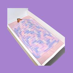 a crocheted baby blanket in a white box on a purple background with an orange butterfly