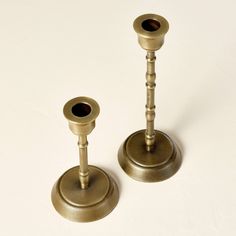 two brass candlesticks on a white surface