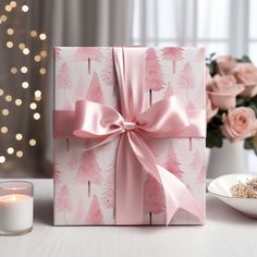 a pink present wrapped in paper and tied with a bow next to a lit candle