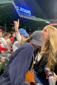 two women are sitting in the stands at a baseball game and one is holding her hand up