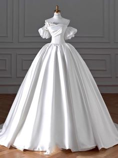 a white wedding dress on a mannequin in front of a gray wall and wooden floor