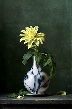 a white and blue vase with a yellow flower in it