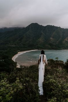 a woman standing on top of a lush green hillside next to a body of water