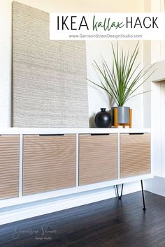 an ikea wall hanging next to a white cabinet with wooden drawers and two plants on top