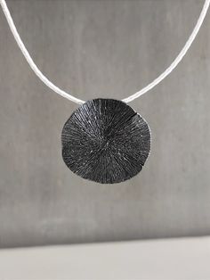 "This round pendant necklace is a stunning and unique handmade piece of 925 sterling silver. The pendant is designed in the shape of a wavy circle with an engraving on its surface and is passed on a white silk cord with a handmade hook clasp, you can choose a different color as shown in the photo black, red, gray. A black and white statement necklace for all time classic looks! DESCRIPTIONS and MEASUREMENTS: Materials: Oxidized sterling silver. Diameter:approx 3,4 (cm) 1,34 (in)\". Length cord: 41,0 (cm) 16,14 (in)\". SEE MORE NECKLACES HERE: www.etsy.com/shop/ArtisJewels?ref=seller-platform-mcnav§ion_id=35815722 Visit my Etsy shop, ArtisJewels, to see more necklaces and jewelry and other unique handmade pieces. www.etsy.com/shop/ArtisJewels Do not hesitate to contact me for any questions Black Necklace With Coin Pendant As Gift, Black Necklace With Coin Pendant For Gift, Artisan Round Sterling Silver Necklace, Unique Oxidized Round Pendant Necklace, Black Coin Pendant Jewelry, Minimalist Necklace With Oxidized Finish, Modern Coin Pendant Necklace As Gift, Modern Handmade Sterling Silver Necklace, Minimalist Necklaces With Oxidized Finish