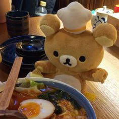 a teddy bear is sitting next to a bowl of soup with an egg in it