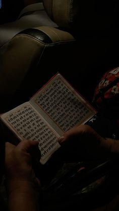 a person is holding an open book in their hands while sitting on a couch at night