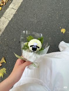 a person holding a flower bouquet with a sheep face on the front and green leaves around it