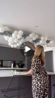 a woman standing in front of a kitchen counter with lots of balloons hanging from the ceiling