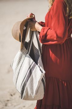 a woman in a red dress carrying a white and black tote bag on the beach