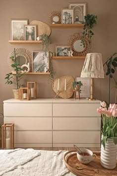 a white dresser topped with lots of vases filled with flowers next to pictures on the wall